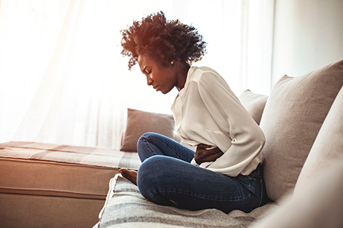 Frau mit Bauchschmerzen durch Reizdarmsyndorm auf dem Sofa